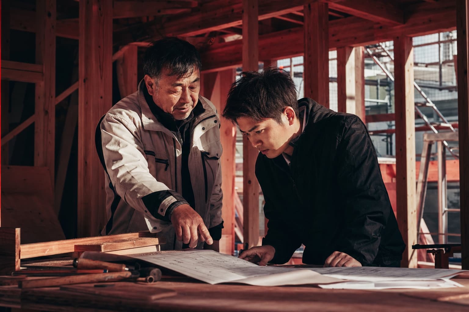 住宅現場で先輩から図面と作業を学ぶ若手職人